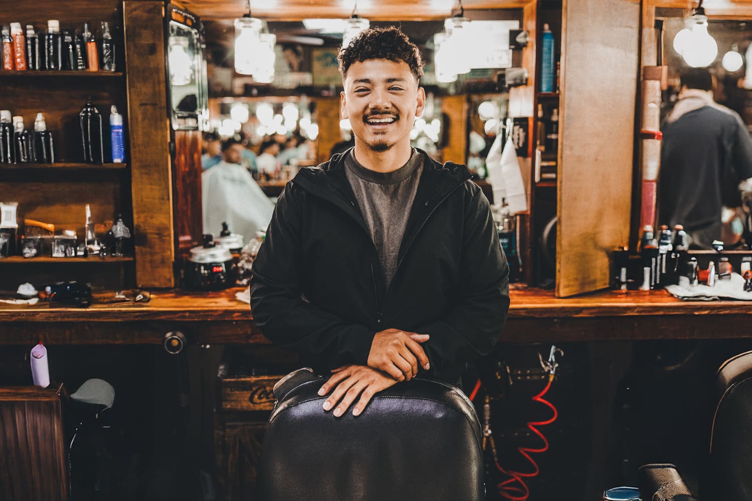 Osiel Campos Jr standing behind his barber chair, with an overlay of his Ad Armory website